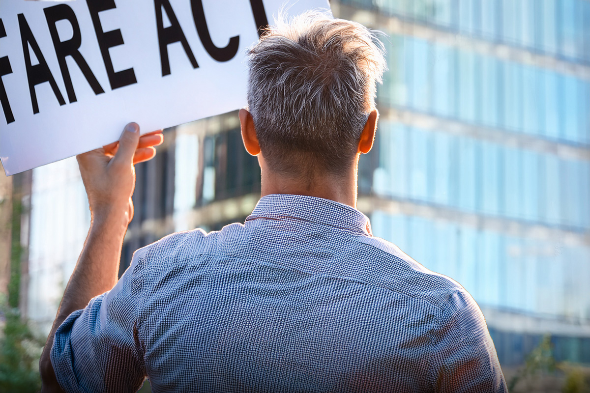 Man holding a FARE Act sign facing a modern luxury condo building in NYC